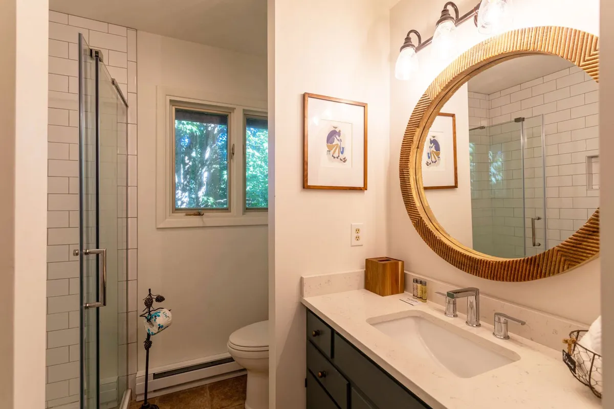 A modern bathroom with a large round mirror, sleek vanity with sink, and a glass shower enclosure. The design is clean and refreshing, emphasizing both style and functionality for daily routines or unwinding after a long day.