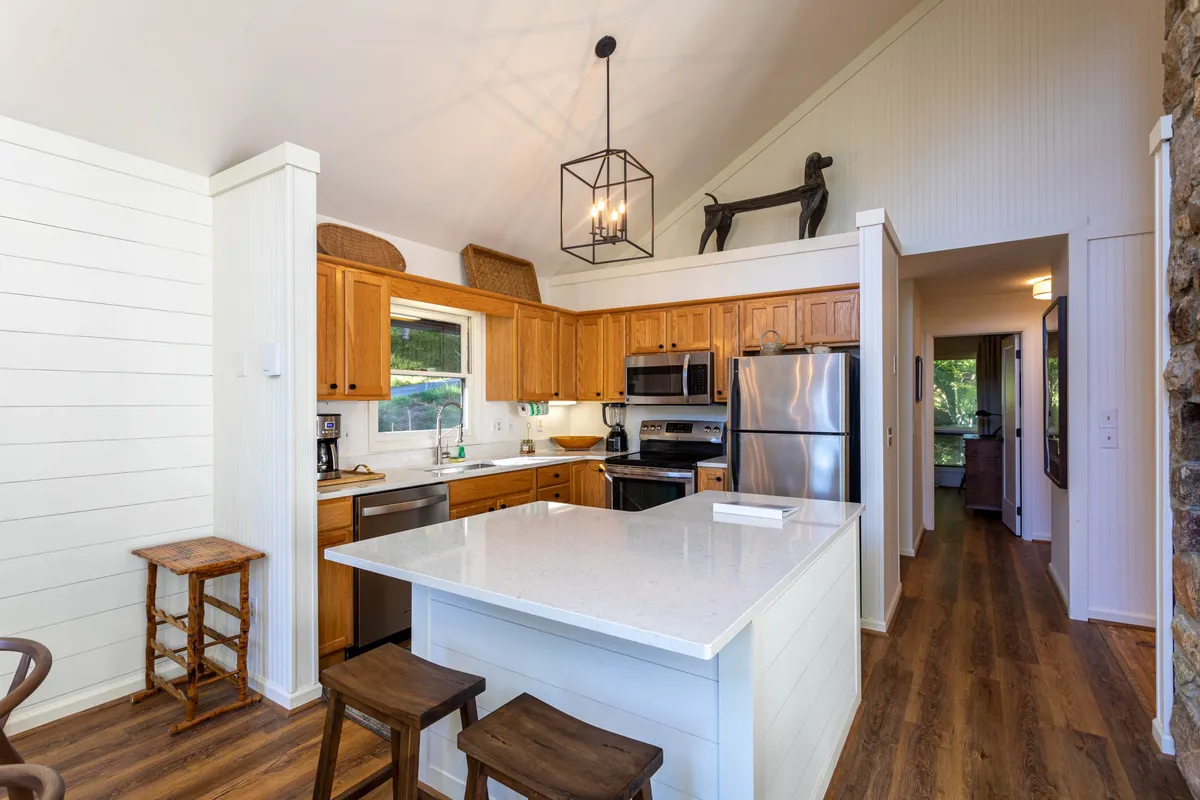 The image showcases a well-equipped kitchen with a spacious island, stainless steel appliances, and warm wooden cabinetry. The lighting is cozy and welcoming, suggesting a space ideal for cooking and gathering. The kitchen’s layout is open, allowing for social interaction during meal preparation.