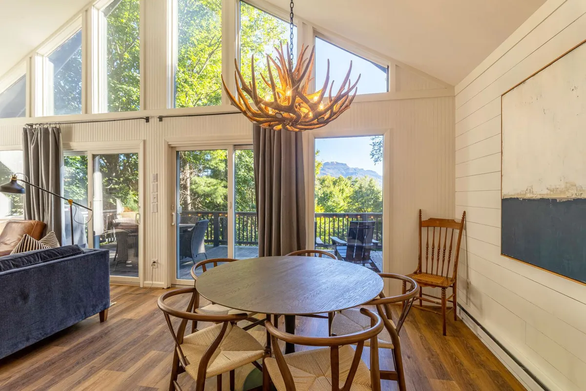 A welcoming dining area with a chandelier overhead, a dining table set for friends or family, a cozy sofa, and wide windows allowing in soft, natural light. The scene hints at memorable meals, social gatherings, and a comfortable retreat no matter the season.